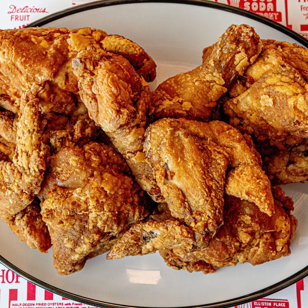 A white plate filled with crispy, golden-brown fried chicken pieces, on a red and white patterned tablecloth.