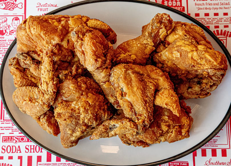 A white plate filled with crispy, golden-brown fried chicken pieces, on a red and white patterned tablecloth.